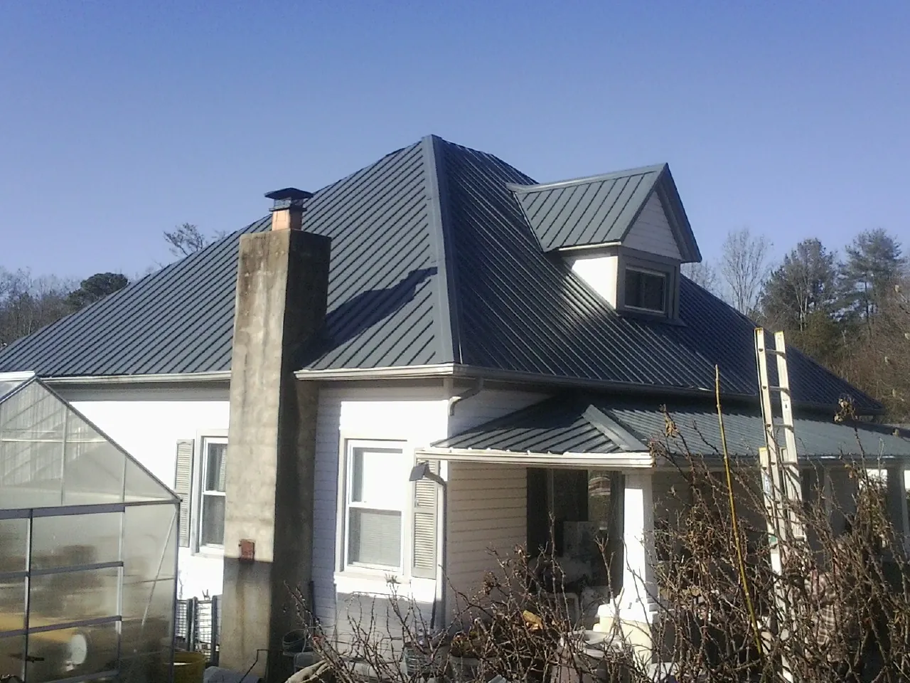 Dark blue standing seam metal roof on a white farmhouse with dormer — Slate & Tile Roof Repair by Roofing Brothers in Stillwater