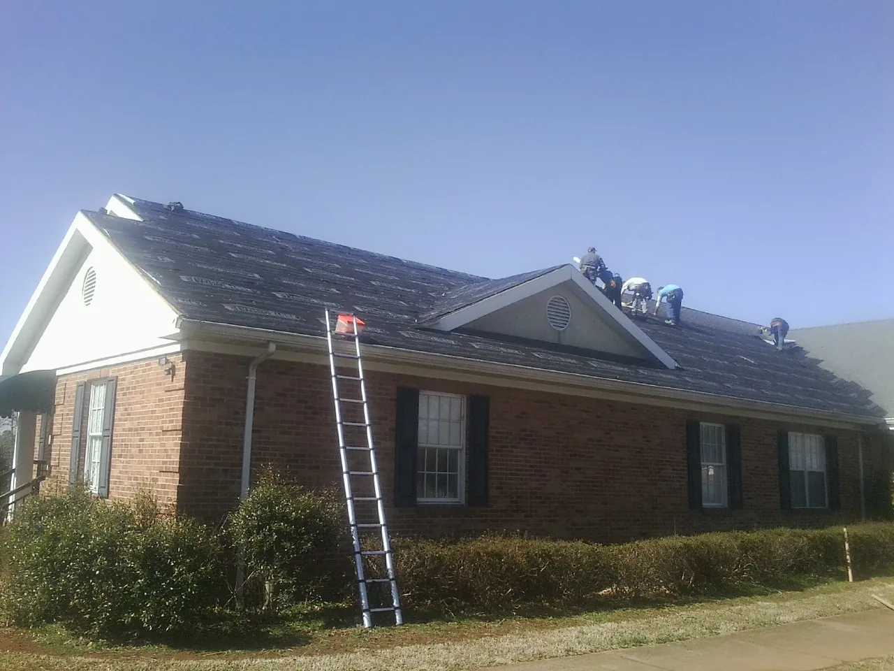 Crew tearing shingles off a brick ranch roof with a ladder set — Metal Roof Repair work by our crew in Stillwater