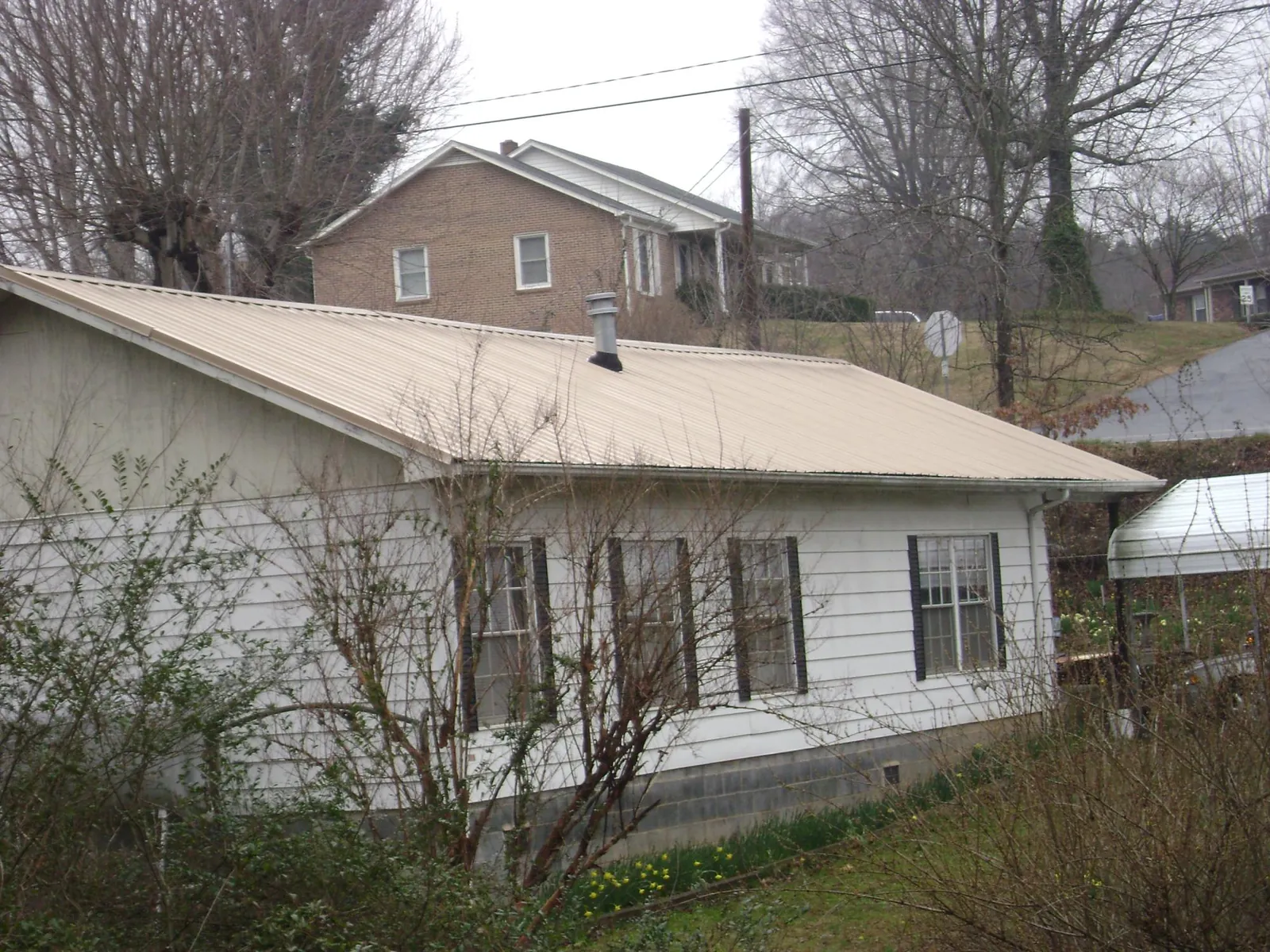 Tan metal roof on a white sided house set into a hillside — Commercial Roofing by Roofing Brothers in Stillwater