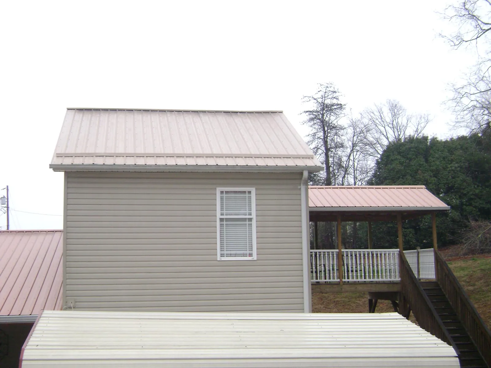 Tan metal roofs on a two story addition and attached porch, from a Roof Replacement job in Stillwater
